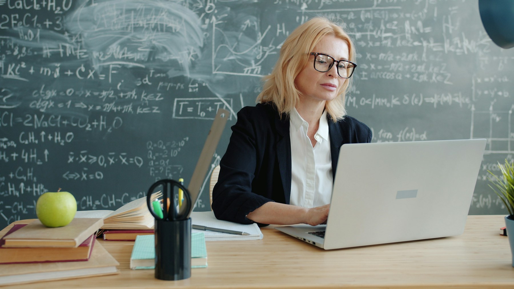 Lektor připravuje výuku a pracuje s notebookem před tabulí